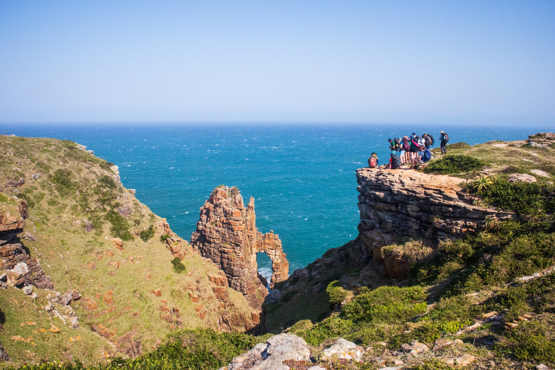 Hikers gathered on a cliff edge above Cathedral Rock arch on the Wild Coast